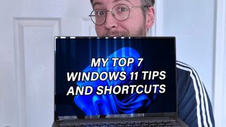 Ben Wilson of Windows Central holding a laptop with "MY TOP 7 WINDOWS 11 TIPS AND SHORTCUTS" displayed on the screen