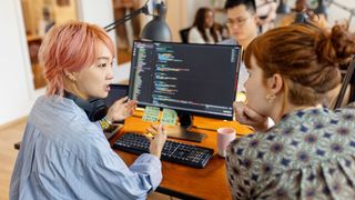 Two women sat in front of a computer with coding software on the screen