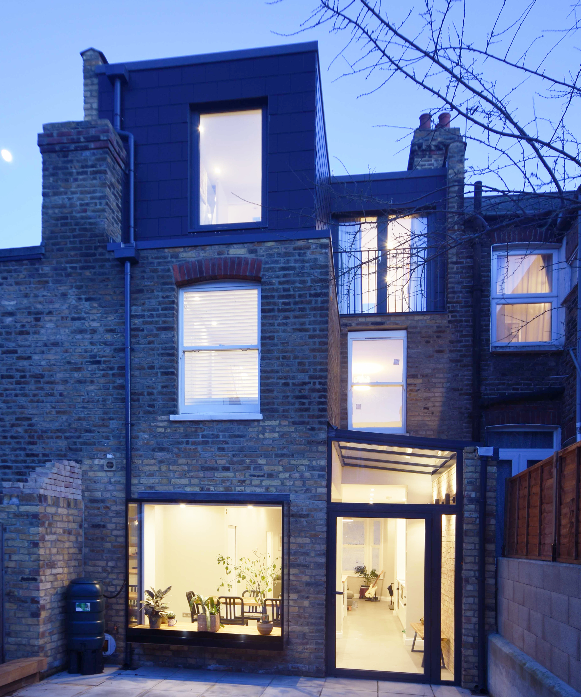 night time shot of rear extension and loft conversion on brick terraced property with rooms inside litup