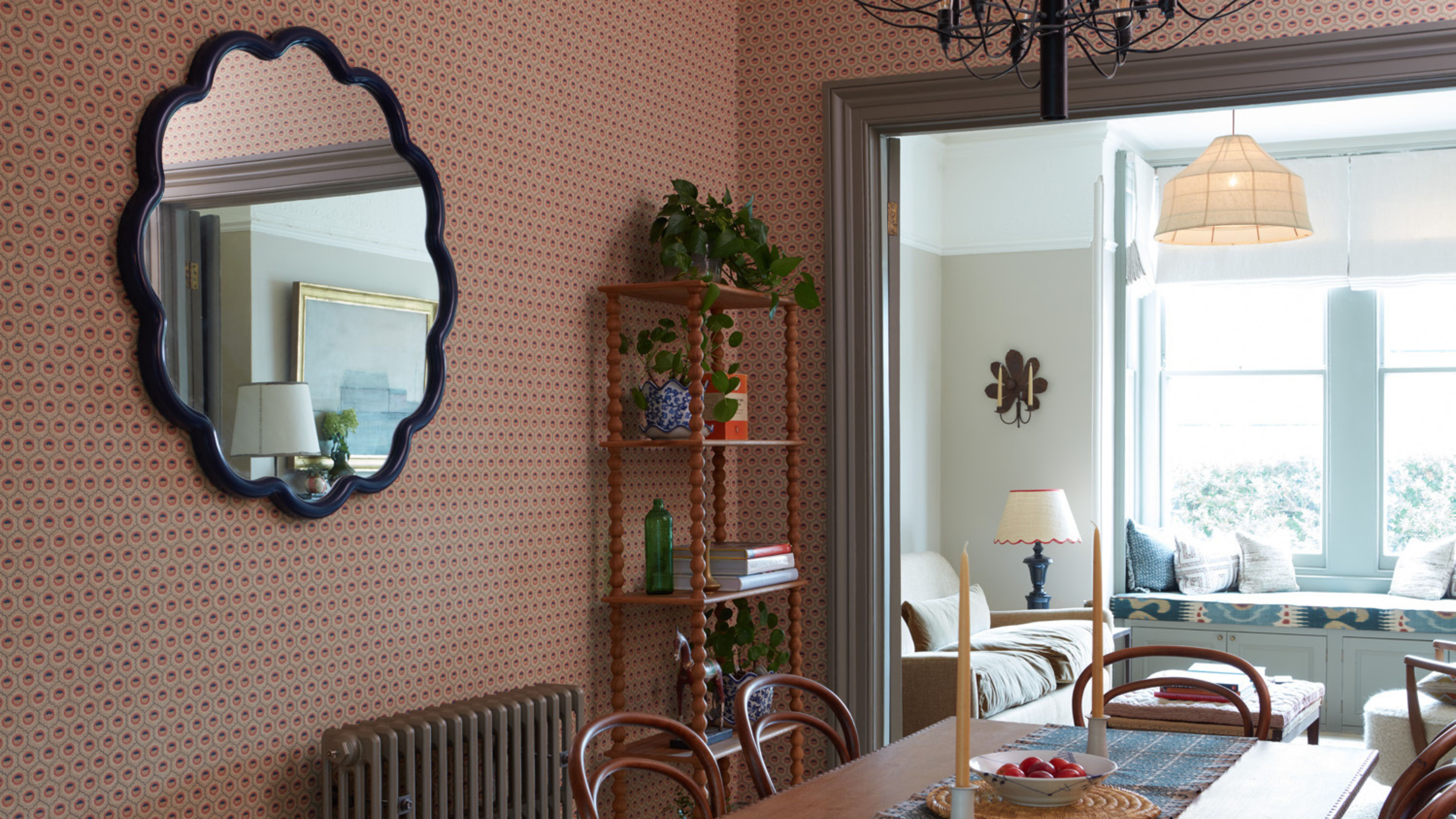 Wavy accent mirror hanging in a dining room with wooden furniture and geometrically patterned wallpaper