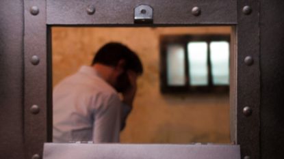 Man holding his head in his hands in a prison cell