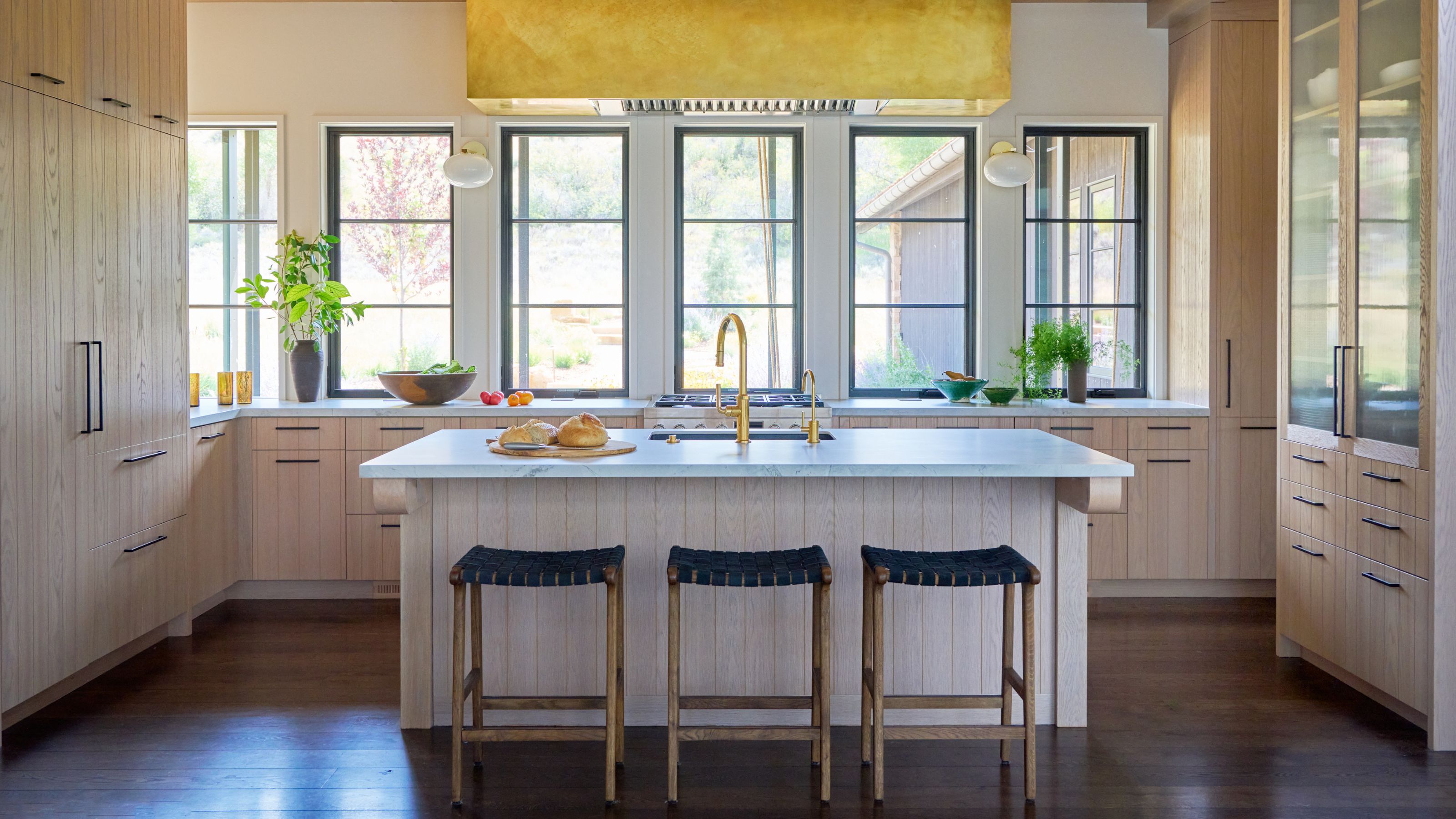 Light and open kitchen with pale wooden cabinets and an island with white worktops. The range hood is covered in bronze.