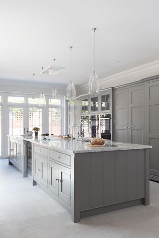 Kitchen with gray island and wall of cabinets, pendant lights, and stone floor