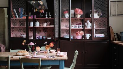 dining room kitchen with large custom cabinets with wallpaper interior/shelving, kitchen table with mint green painted chairs, flowers, vases, Farrow &amp; Ball 