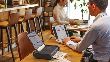 Man at shared desk using his laptop next to the best compact printer 