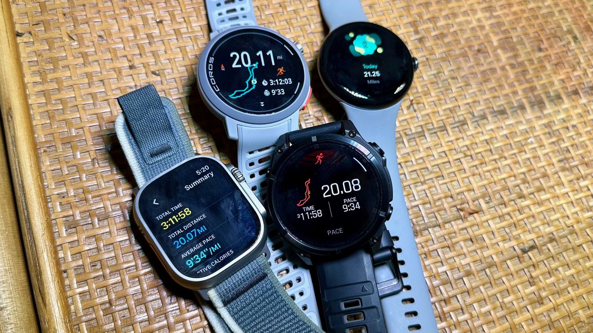 The Apple Watch Ultra 2, Garmin Fenix 8, COROS PACE Pro, and Google Pixel Watch 3 sitting on a bookshelf together, all showing a post-run summary for a 20-mile race that day.