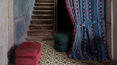 a entryway with a patterned curtain with a tieback and a patterned floor, the stairs are a rustic wood