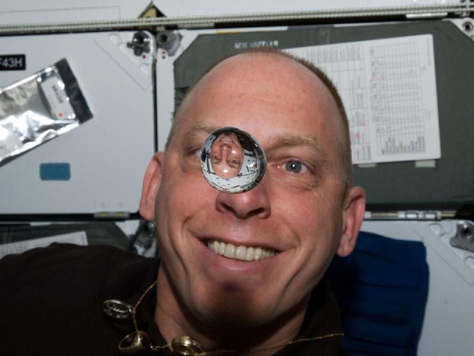 NASA astronaut Clayton Anderson floats on the middeck of space shuttle Discovery during the STS-131 mission in April 2010. In front of him is a water bubble that reflects an upside-down image of the spaceflyer because the light has been refracted.