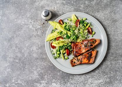 A photo showing what to eat after a workout with a plate of salmon with a tomato, broccoli and green leaves.