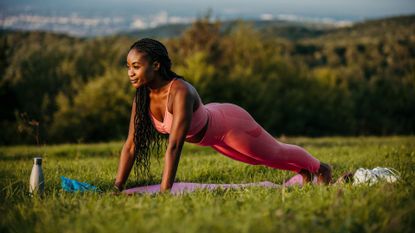 A woman performing an inch worm on a yoga mat in a grass field