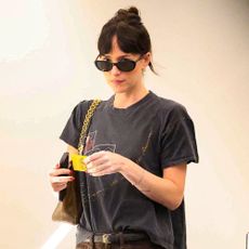 Dakota Johnson walks through an office building wearing brown baggy jeans with a black graphic t-shirt.