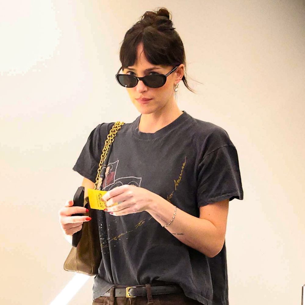 Dakota Johnson walks through an office building wearing brown baggy jeans with a black graphic t-shirt.