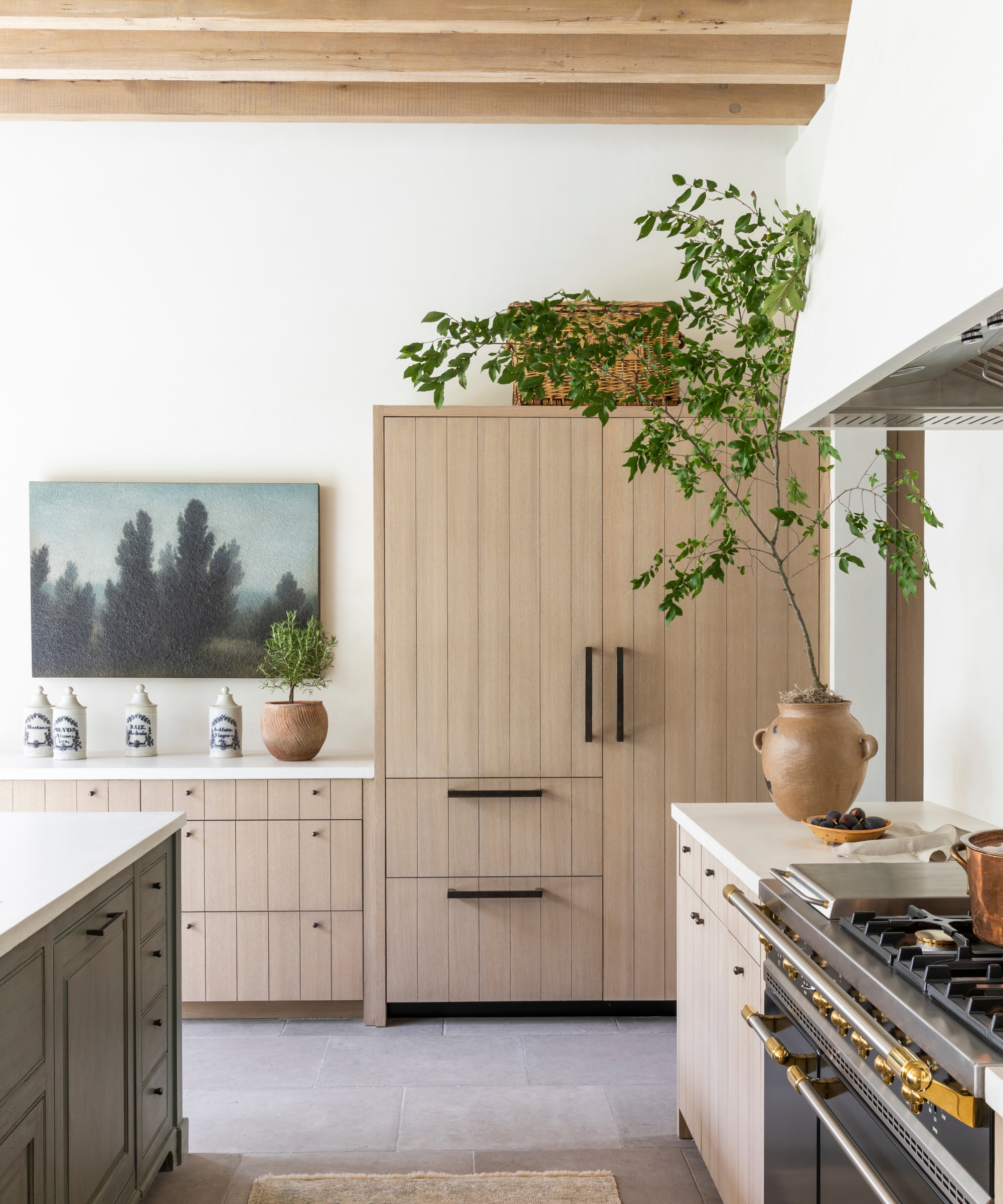 A close up of the paneled wood cabinets in a neutral kitchen, with a large landscape artwork on the wall
