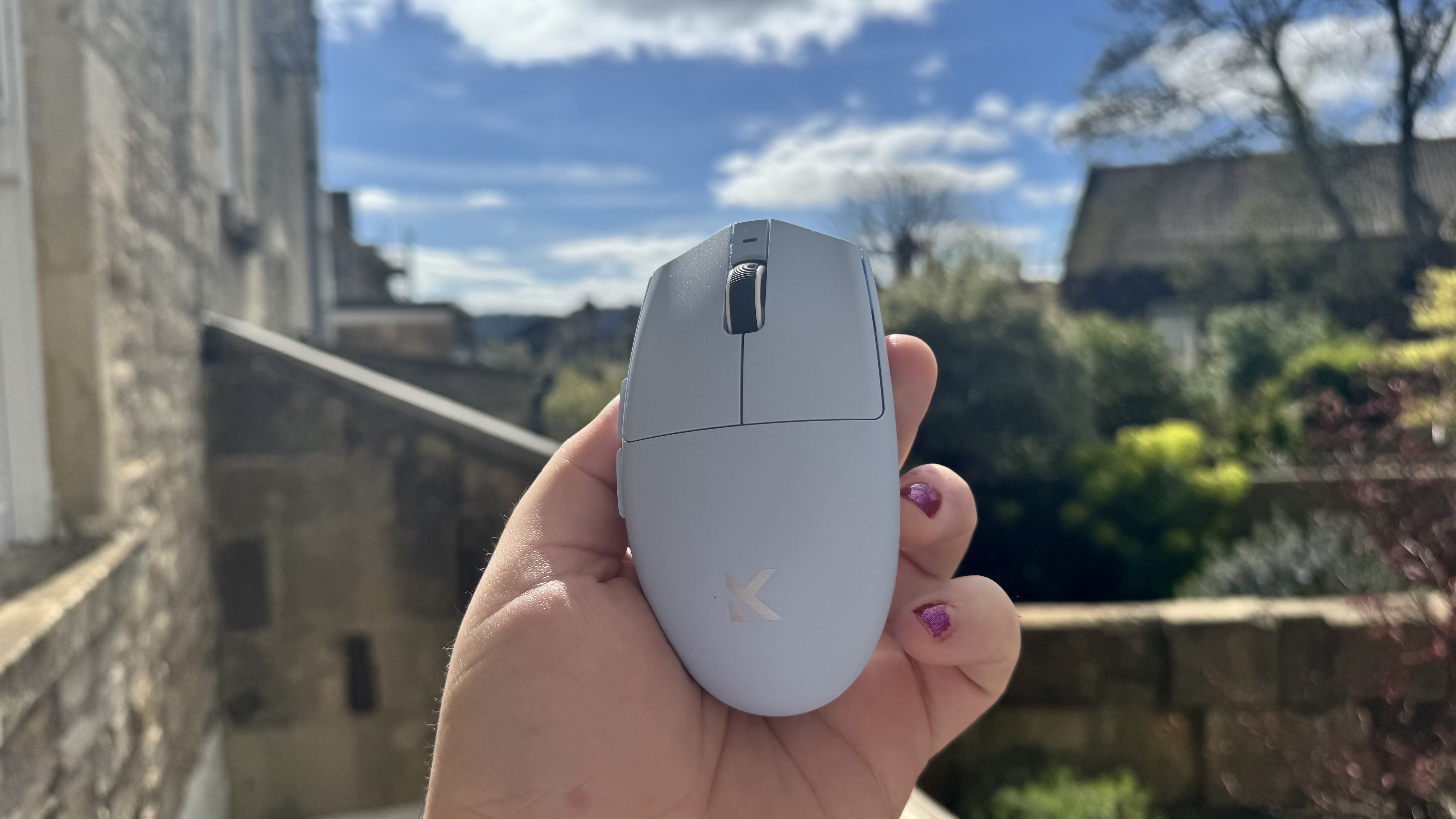 The blue Mchose G3 V2 gaming mouse from the top, in a hand in a garden