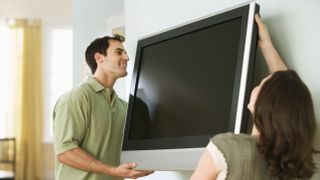 A couple mounting a tv to a wall with the man smiling