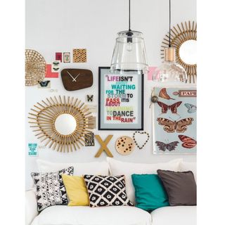 Collection of mirrors, clocks and frames on a white wall behind a white couch with eclectic assortment of colored and patterned cushions