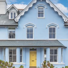 Victorian house with pitched roof and white gables, pale blue painted render and yellow front door, with porch