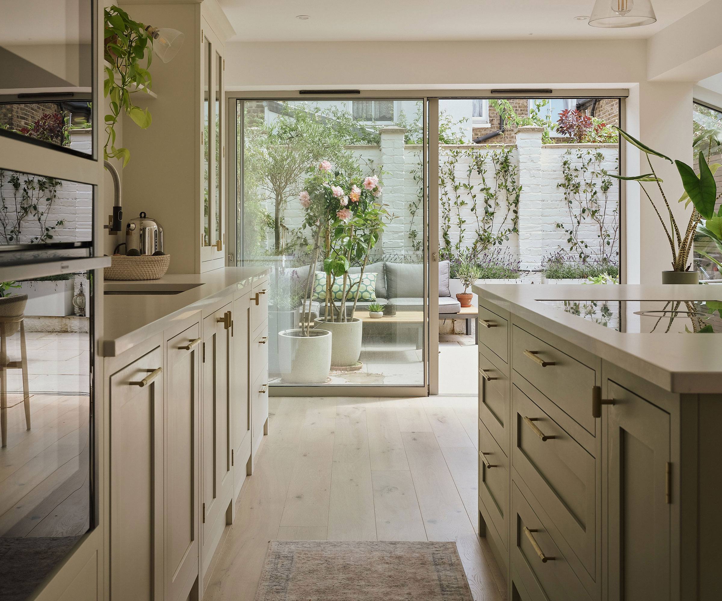 Shaker kitchen with pale wooden flooring and sliding doors to courtyard