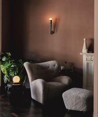 chocolate brown living room with fluffy boucle chair and footstool, hardwood floor, plant, fireplace, wall light