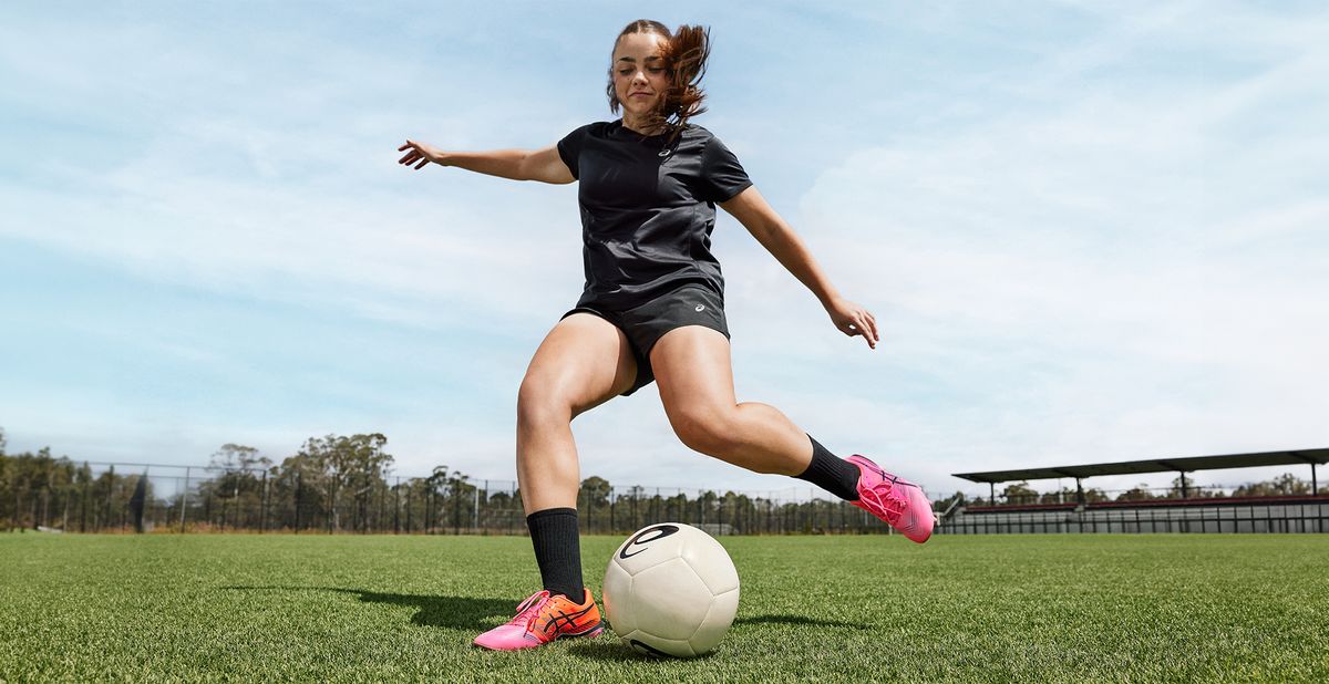 A female footballer wearing Asics football boots striking a ball