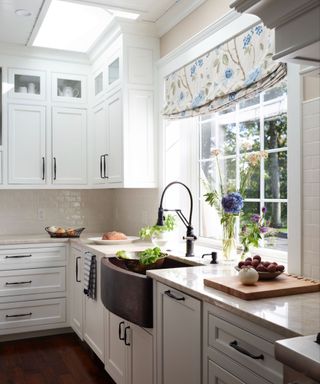 A white kitchen with blue floral curtains and a copper sink