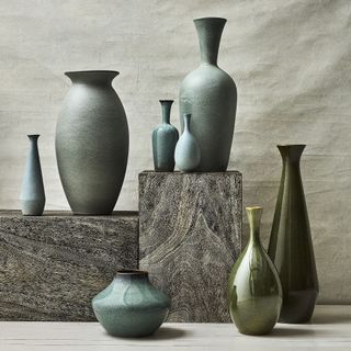 A collection of blue-green vases in varying shapes situated on and around grey stone platforms