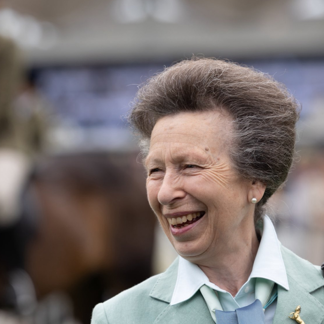 Princess Anne wearing a mint green blazer with a horse rider in the background