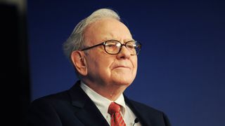 Warren Buffet in a suit, against a blue backdrop