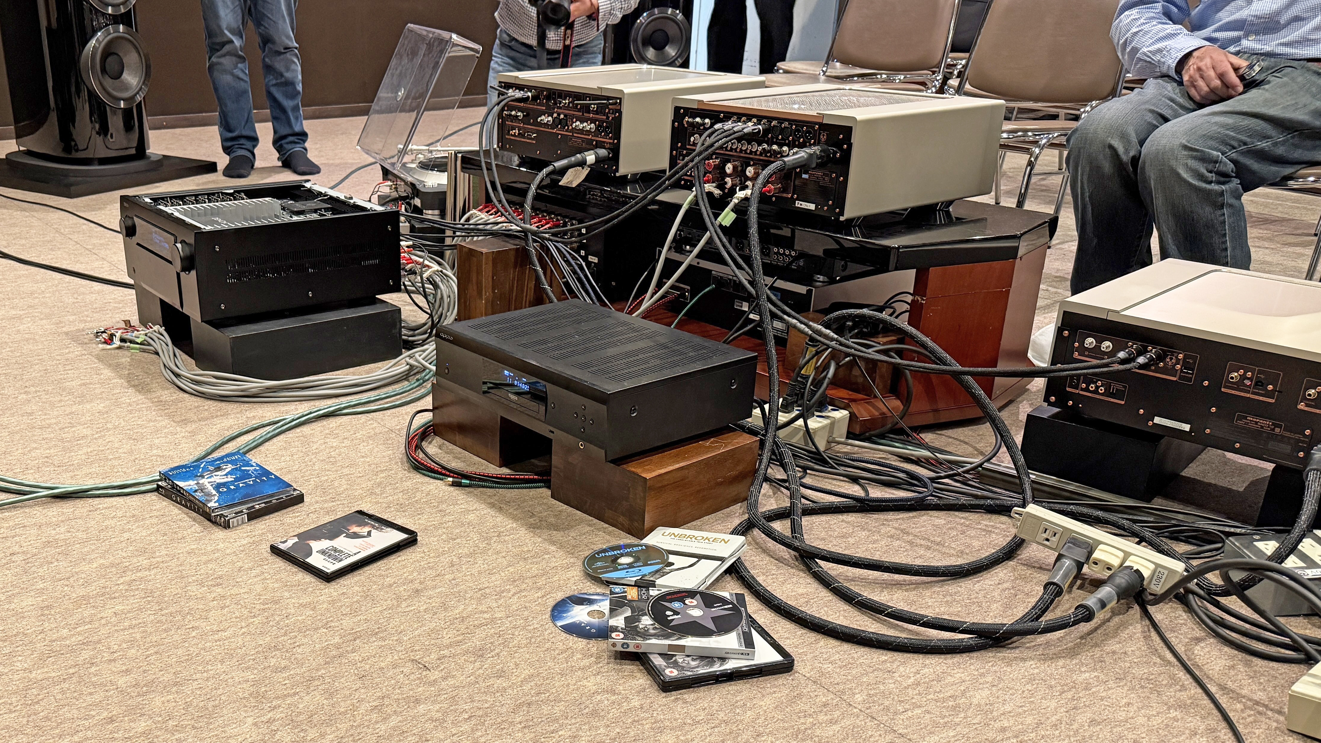 The interior of a home theater listening room with multiple pieces of AV equipment next to each other, all with a mass of cables in and out