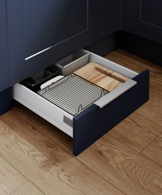 A dark blue kitchen with a storage drawer hidden in the plinth and wooden flooring.