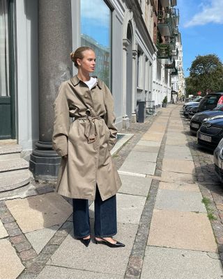 Scandinavian woman wearing a stylish spring outfit with a trench coat, dark denim, and slingback heels