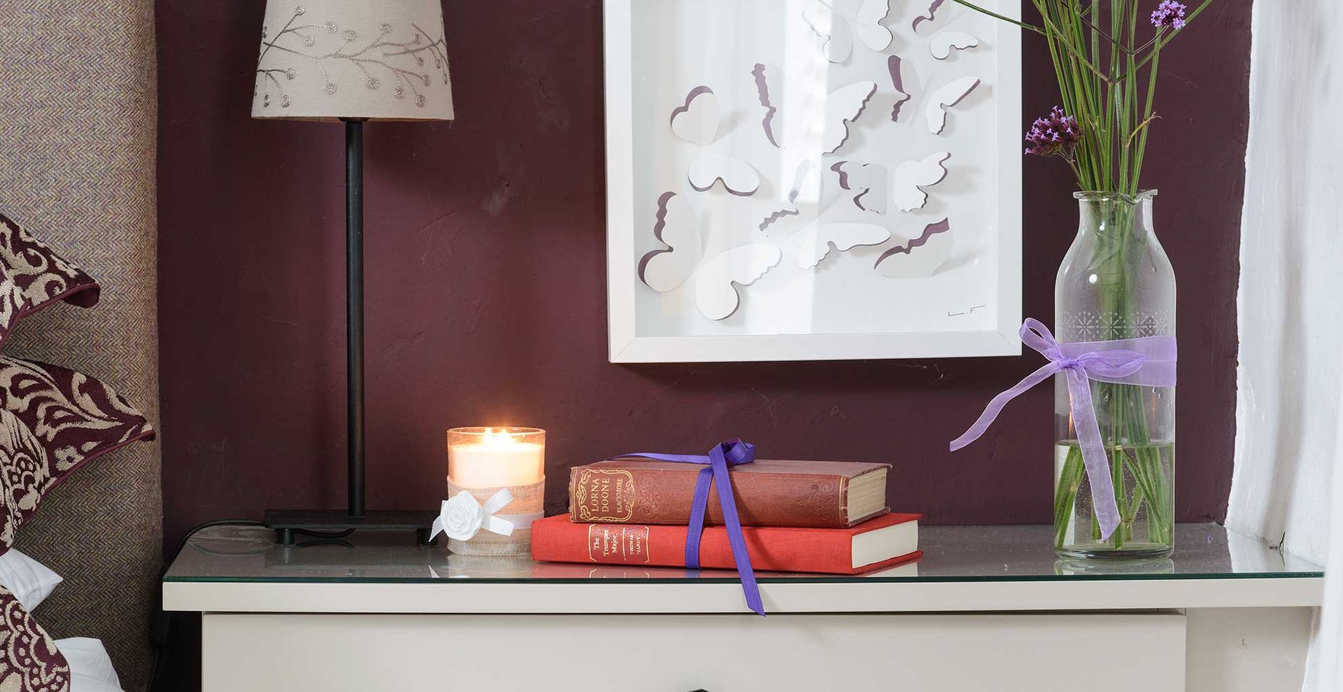 plum coloured bedroom with dresser beside a bed with a candle to demonstrate scent-scaping in a bedroom