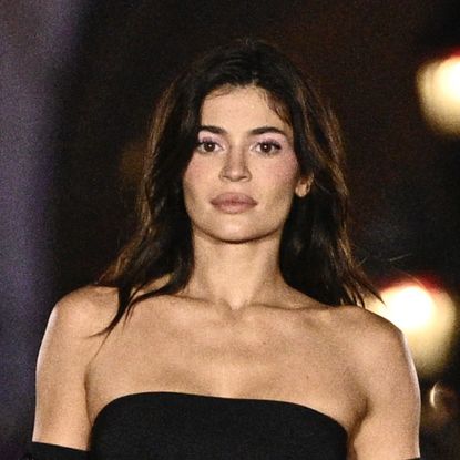 Kylie Jenner wears a strapless black gown and long black gloves as she walks the runway in front of the Disney castle