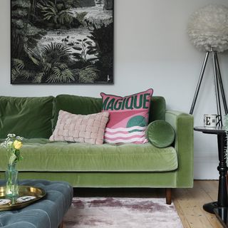 A living room with a green velvet sofa with contrasting cushions, a light purple rug and a quilted blue ottoman