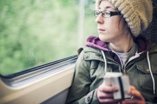 Teenage girl sat on a train holding a train ticket and her phone, looking out of the window