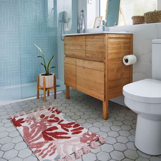 White marble walled bathroom with wooden cabinet sink, white toilet, and colourful tufted small rug