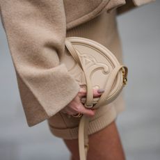 Alison Toby wears a beige wool oversized jacket from Patou, a beige wool t-shirt from Patou, beige wool shorts from Patou, a beige matte leather shiny leather handbag from Celine with sheer brown nails