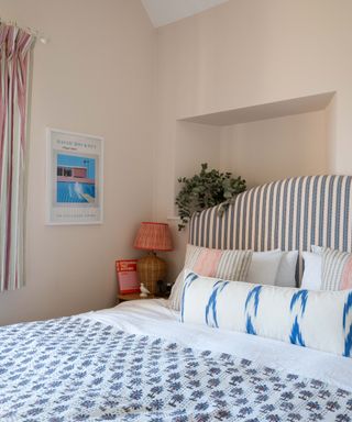 corner of bedroom with pale pink walls and blue patterned bedding and striped headboard