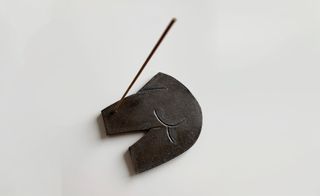 View of an incense stick in a dark brown incense burner by Ludovic de Saint Sernin pictured against a light coloured background