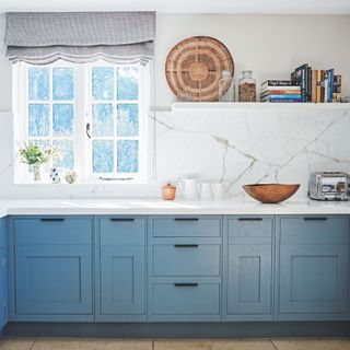 White marble kitchen with blue cabinets and a wooden window behind it