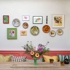 White wall with pink bench and multi-coloured plate wall with flowers on table