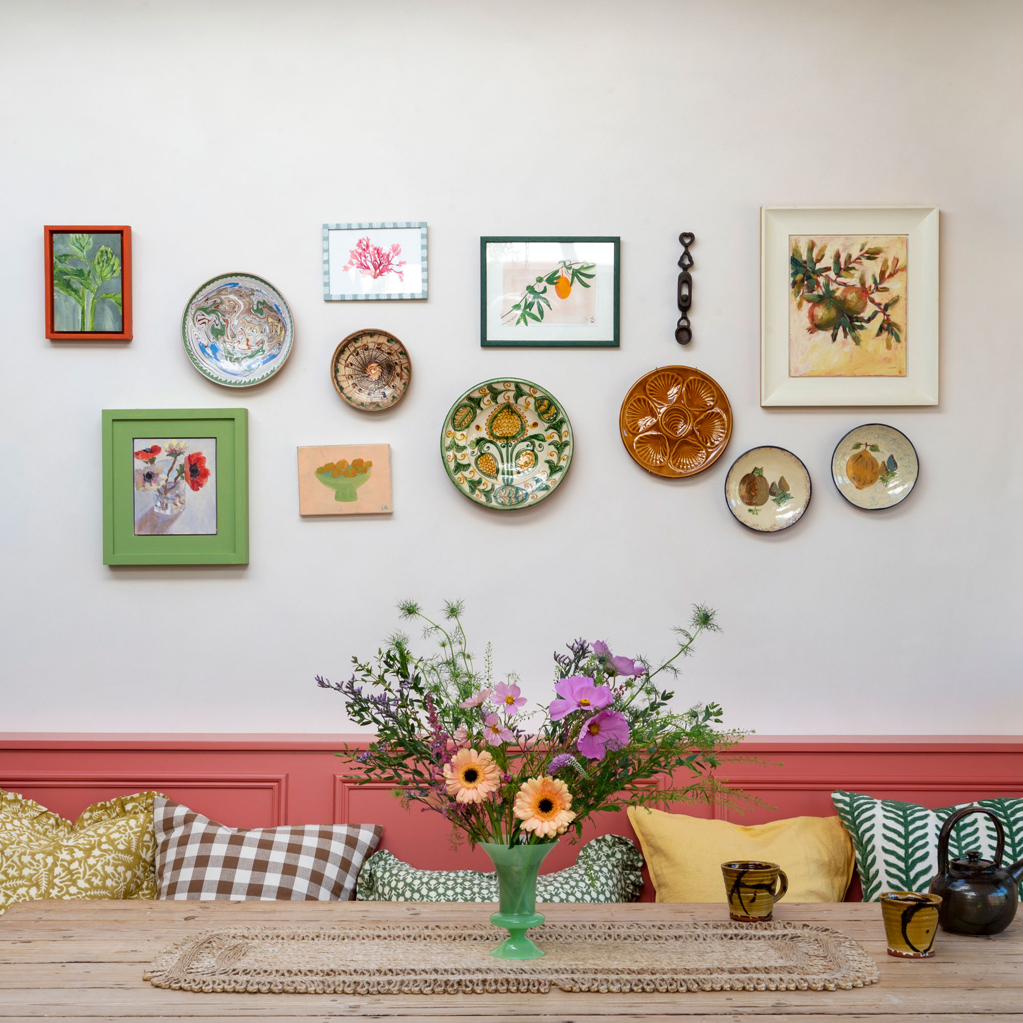 White wall with pink bench and multi-coloured plate wall with flowers on table