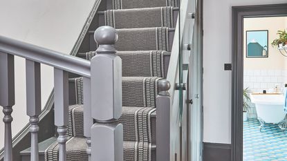 A grey staircase with a black and white stair runner leading into a hallway