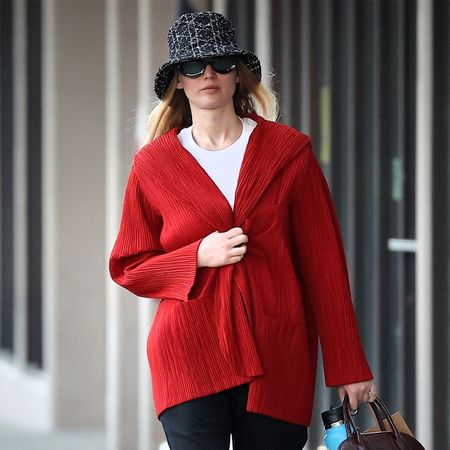 Jennifer Lawrence wears a burgundy bag, a red cardigan, white t-shirt, black bucket hat, black pants, and black sneakers.