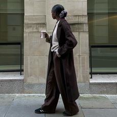 model wears sweater, coat, trousers, and sneakers