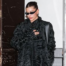 Hailey bieber wears a black ruffled coat and black sunglasses.