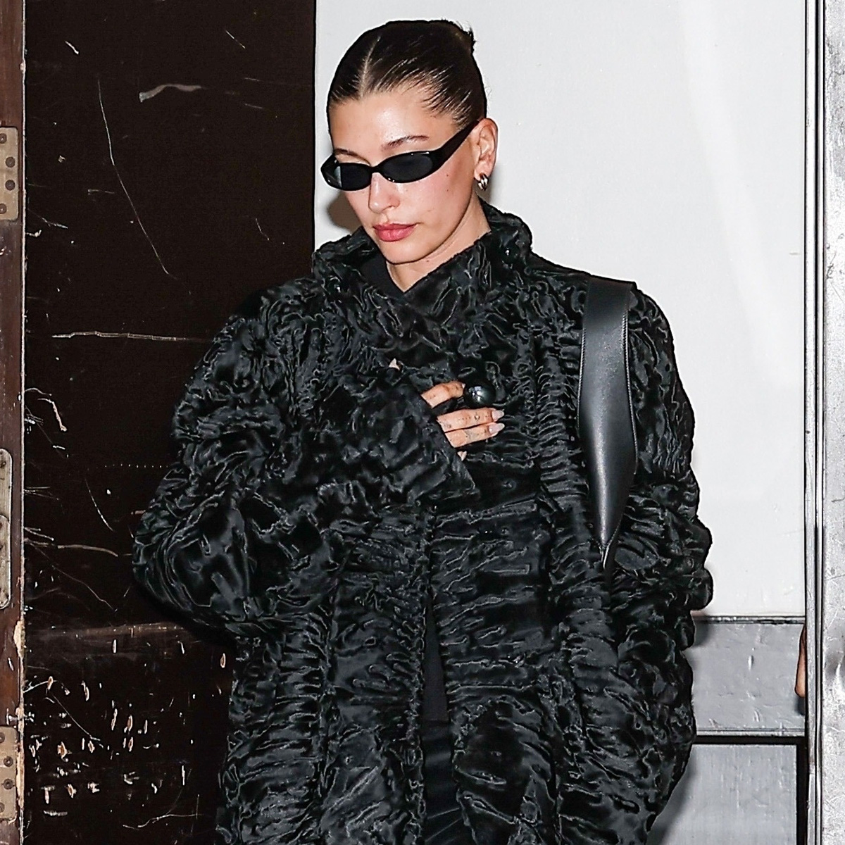 Hailey bieber wears a black ruffled coat and black sunglasses.