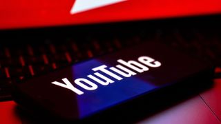 The YouTube logo is displayed on a mobile phone screen above a computer