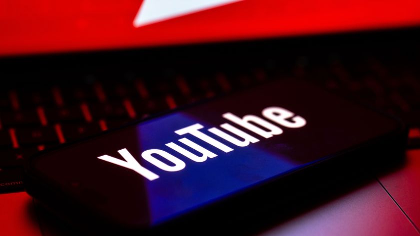 The YouTube logo is displayed on a mobile phone screen above a computer