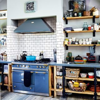 kitchen with white tiles, a blue oven, wooden shelves with mugs and bowls
